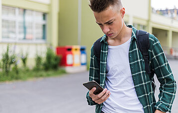 Jugendlicher auf dem Schulhof schaut besorgt auf sein Handy. 