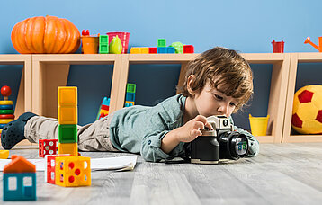 Ein kleiner Junge im Kindergartenalter liegt auf dem Boden und fotografiert etwas mit einer Kamera