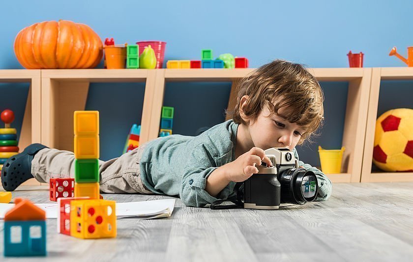 Ein kleiner Junge im Kindergartenalter liegt auf dem Boden und fotografiert etwas mit einer Kamera