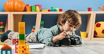 Ein kleiner Junge im Kindergartenalter liegt auf dem Boden und fotografiert etwas mit einer Kamera