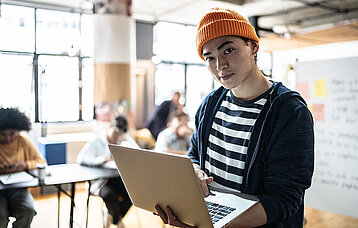 Porträt eines jungen Mannes, der den Laptop im Klassenzimmer oder in einem kleinen Unternehmen hält.