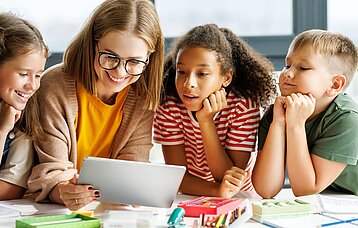 Grundschullehrerin zeigt drei Schülerinnen und Schülern ein animiniertes Bilderbuchkino auf einem Tablet.
