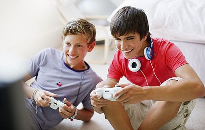 Zwei Teenager-Jungs sitzen auf dem Boden und halten Controller für eine Computerspielkonsole in der Hand. 