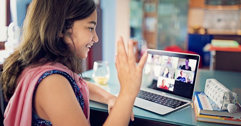 Mädchen winkt bei einer Videokonferenz in den Bildschirm