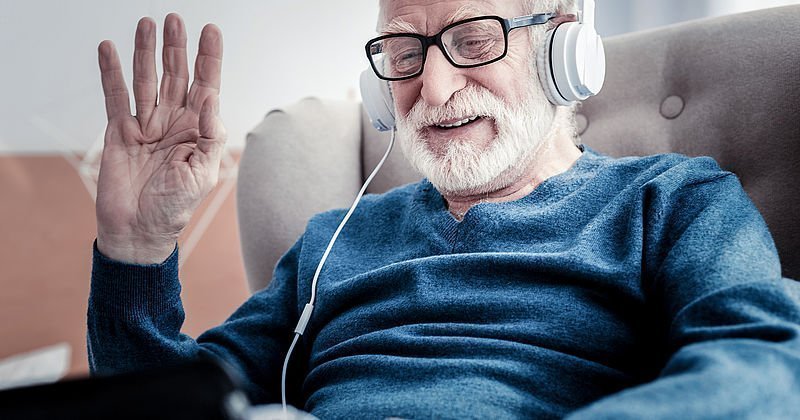 Älterer Mann mit Kopfhörer schaut auf sein Tablet