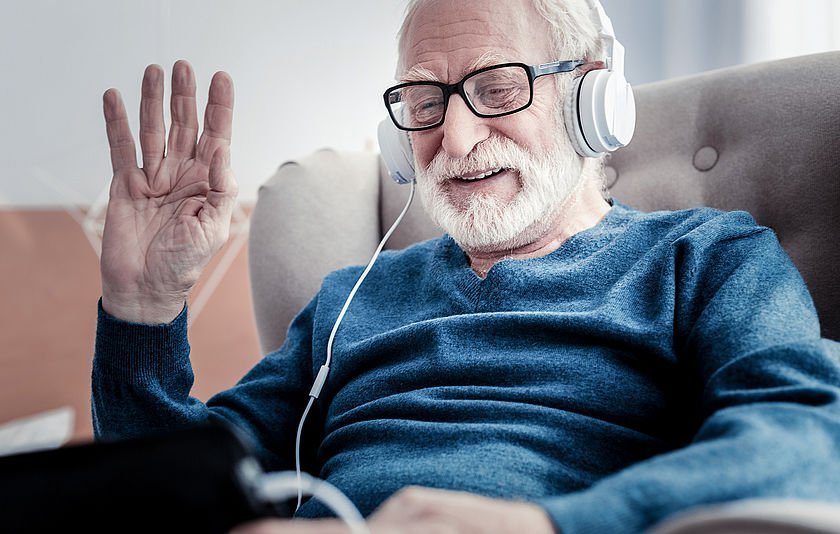 Älterer Mann mit Kopfhörer schaut auf sein Tablet Älterer Mann mit Kopfhörer schaut auf sein Tablet