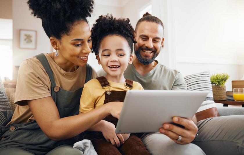 Eltern mit Kind im Kindergartenalter sitzen auf dem Sofa und schauen gemeinsam auf ein Tablet.