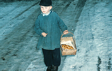 Kinderschüler im Blauhemd beim "Klopfen". Im Korb das Hefezöpfchen seiner "Dote", (Patin), 1955. Fotografie von Eugen Sauter.