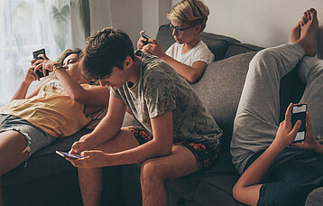 Vier Jugendliche hängen auf dem Sofa rum und schauen in ihr Smartphone.