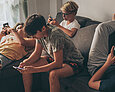 Vier Jugendliche hängen auf dem Sofa rum und schauen in ihr Smartphone.