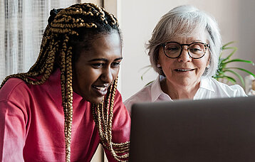 Zwei Frauen aus mehreren Generationen sitzen gemeinsam am Computer und führen einen Videoanruf durch. 