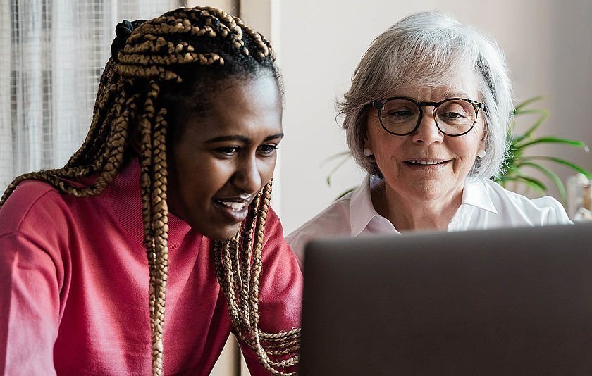 Zwei Frauen aus mehreren Generationen sitzen gemeinsam am Computer und führen einen Videoanruf durch. 