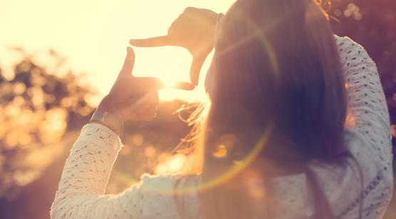Mädchen macht mit vier Fingern ein Rechteck vor dem Sonnenuntergang
