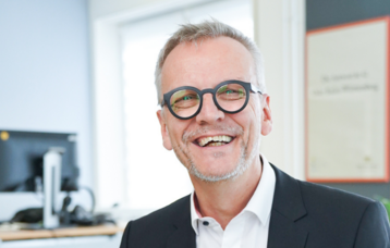 Man sieht Michael Zieher, den Direktor des LMZ. Ein Mann mit grauen Haaren und Brille leachelt in die Kamera.