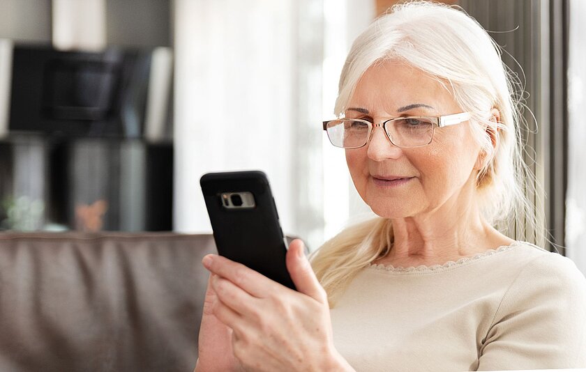 Ältere Dame liest Nachrichten auf ihrem Handy.