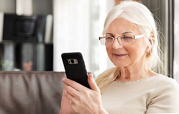 Ältere Dame liest Nachrichten auf ihrem Handy.