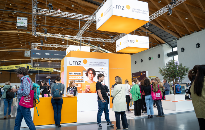 Messestand des LMZ in leuchtendem Orange, davor eine Menschenmenge