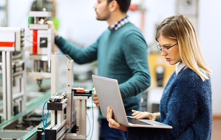 Zwei Personen mit Laptop vor einer großen Maschine