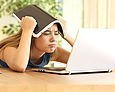 Mädchen legt sich vor einem Laptop ein Heft auf den Kopf
