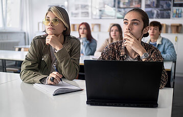 Nachdenkliche Gymnasiasten, die im Klassenzimmer am Computer arbeiten und an einer Aufgabe tüfteln.