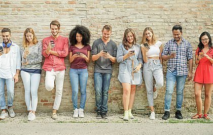 Jugendliche mit Smartphones stehen in einer Reihe vor einer Wand