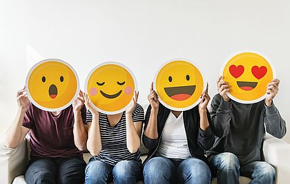 Vier Personen halten unterschiedliche Emojis aus Pappe vor ihr Gesicht.