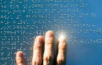 Finger auf einer Metallplatte mit Blindenschrift