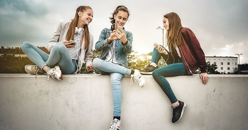 Mädchen mit Smartphones sitzen auf einer Mauer