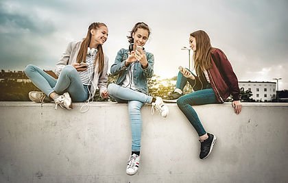 Mädchen mit Smartphones sitzen auf einer Mauer