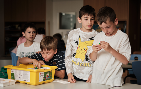 Einige Grundschüler sitzen und stehen gemeinsam um eine LEGO-Box und beschäftigen sich konzentriert mit den Bauteilen. 