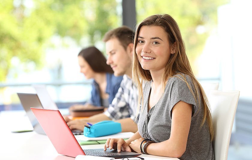 Drei Jugendliche sitzen mit Laptops in einer Reihe vor einem Fenster