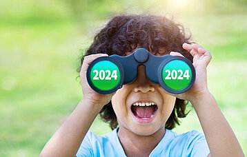 Kleiner, lockiger Junge schaut durch ein Fernglas. Auf der Linse erscheint das Jahr 2024.