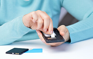 Zwei Hände wechseln eine SIM-Karte am Smartphone