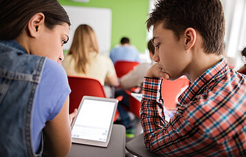 Zwei Kinder im Klassenzimmer zeigen sich etwas auf dem Tablet
