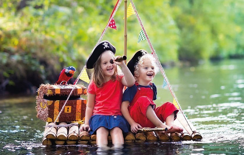 Zwei Kinder mit Piratenhüten sitzen auf einem Floß