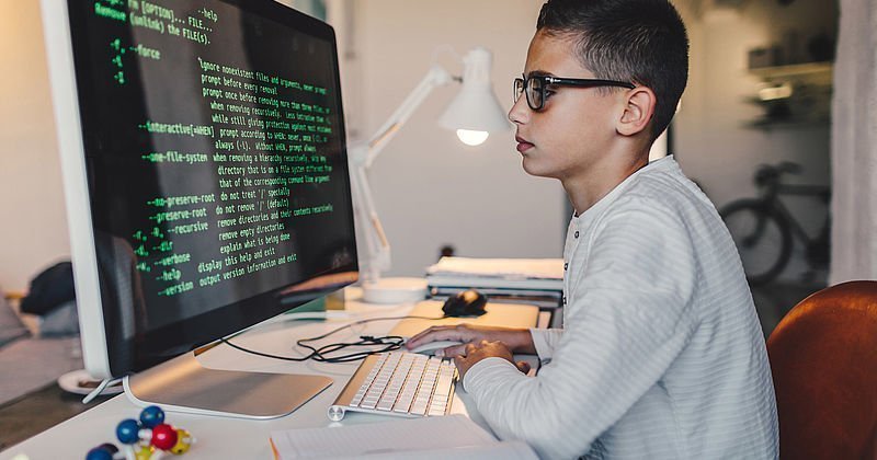 Junge vor einem riesigen Bildschirm mit Programmiersprache