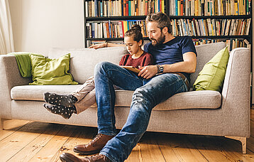 Vater und Tochter mit Tablet auf Sofa