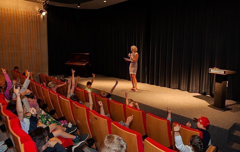 Schülerinnen und Schüler im Kinosaal hören einer Rednerin zu 