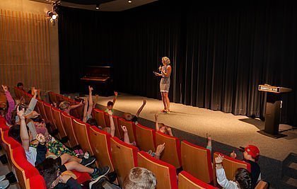 Schülerinnen und Schüler im Kinosaal hören einer Rednerin zu 