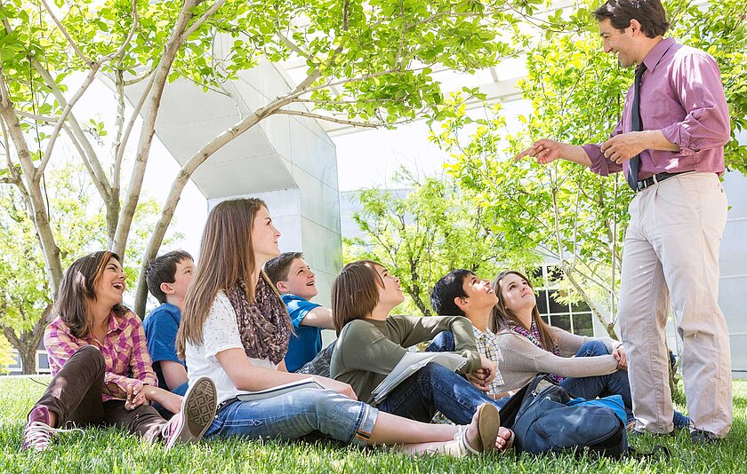 Jugendliche sitzen in einem Park vor ihrem Lehrer.