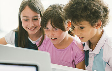 Drei Grundschüler/-innen sitzen fasziniert vor dem Laptop.