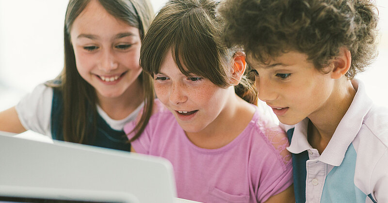Drei Grundschüler/-innen sitzen fasziniert vor dem Laptop.