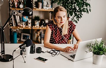 Frau am Laptop mit Standmikrofon und Ohrhörern