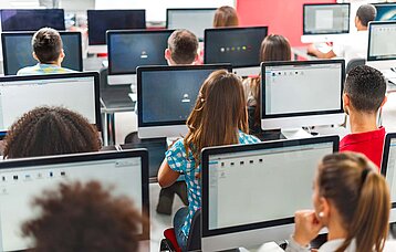 Jugendliche vor PC-Bildschirmen im Klassenzimmer