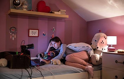 Junge Frau liegt auf ihrem Bett vor einem Laptop