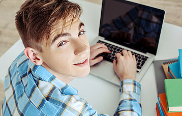 Junge sitzt am Laptop und schreibt