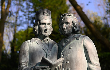 Statue der Brüder Grimm. Einer von beiden hält ein Buch in den Händen.