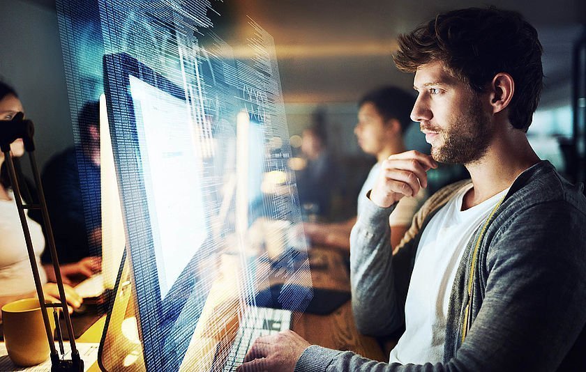 Programmierer vor Bildschirm mit Team im Hintergrund.