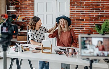 Zwei Frauen sitzen vor einer Kamera und machen Werbung für Beauty-Produkte  