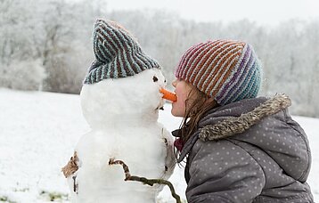 Mädchen, das die Karottennase eines Schneemanns aufisst